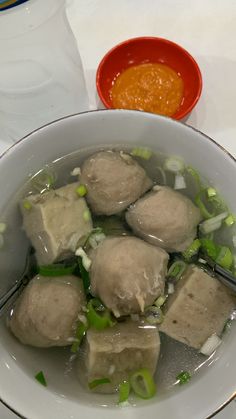 a bowl filled with meat and vegetables next to a container of sauce on a table