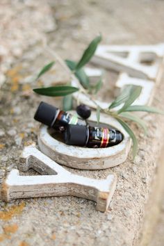 an olive branch with two bottles in it on a stone surface next to a wooden letter