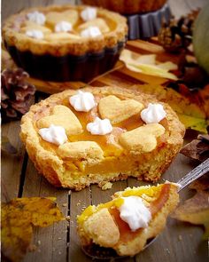 two pies sitting on top of a wooden table next to leaves and pumpkins