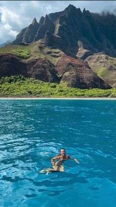 a man is swimming in the ocean with mountains in the backgrouds behind him