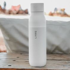 a white water bottle sitting on top of a wooden table next to a pillow in the background