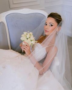 a woman in a wedding dress sitting on a blue chair holding a bouquet of flowers