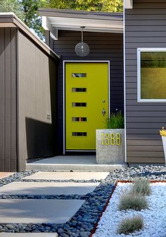 a yellow door sits in front of a gray house with white rocks and gravel on the ground