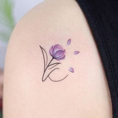 a small flower tattoo on the back of a woman's shoulder, with purple flowers coming out of it