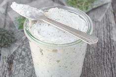 a glass jar filled with white sauce on top of a wooden table next to a spoon