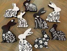 paper cut rabbits sitting on top of a wooden table with white flowers and black silhouettes