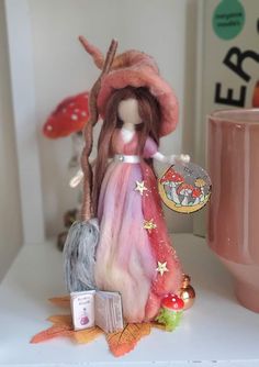 a doll is standing on a table next to a mug and some other items in front of it