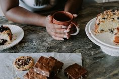 a woman is holding a coffee mug and some desserts on the table with her hands