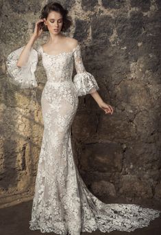 a woman in a white wedding dress standing next to a stone wall with her hands on her head