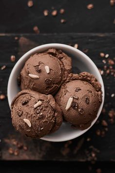 four chocolate ice creams in a white bowl on a black surface with nuts scattered around