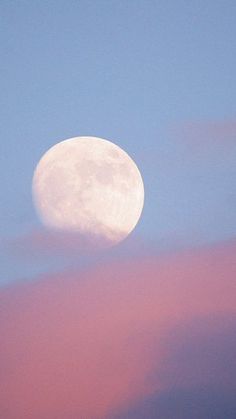 the full moon is seen in the sky with pink clouds around it and blue skies