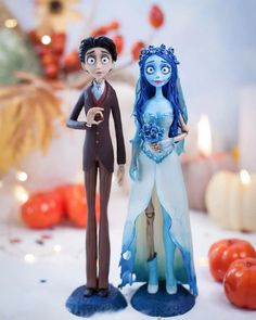 two figurines are standing next to each other in front of some pumpkins