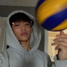 a young man holding a yellow and blue ball in his hand while wearing a hoodie