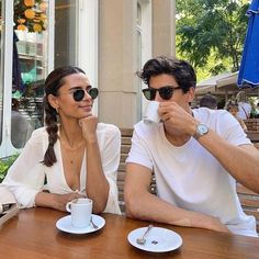 a man and woman sitting at a wooden table with cups of coffee in front of them