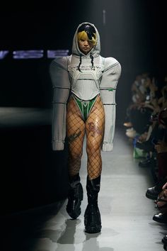 a woman in fishnet stockings and boots walks down the runway