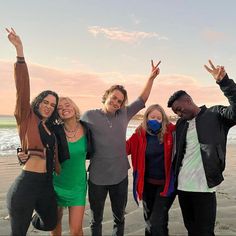 four people standing on the beach with their arms in the air and one person wearing a face mask