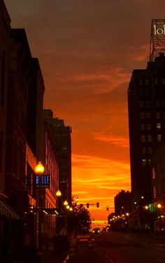 the sun is setting over some buildings and street lights in an urban area with tall buildings