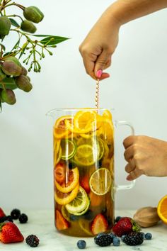 a pitcher filled with lemons, oranges and strawberries being poured into it