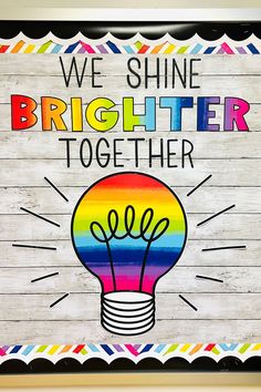 we shine brighter together sign with rainbow lightbulb on wood planks and white background