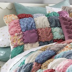 a bed topped with lots of colorful pillows and blankets covered in ruffles on top of each other