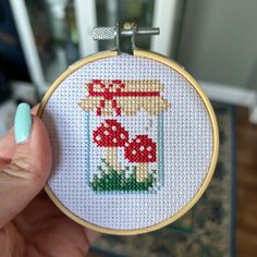 a person holding up a cross stitch project with mushrooms in a jar on the front