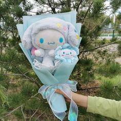 a person holding a stuffed animal in their hand near some pine trees with other items