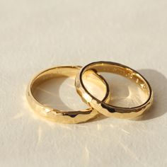 two gold wedding rings sitting side by side on a white tablecloth with light reflecting off the surface