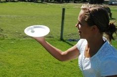 a woman holding a white frisbee in her right hand while standing on top of a lush green field