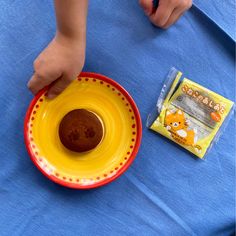 a small child is eating from a yellow and red bowl on a blue tablecloth