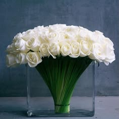 a vase filled with white roses sitting on top of a table next to a wall