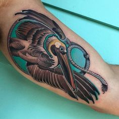 a pelican tattoo on the arm with an eyeball in it's beak