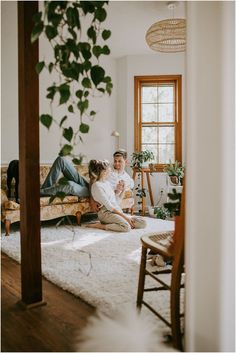 a man and woman sitting on top of a couch in a living room next to a potted plant