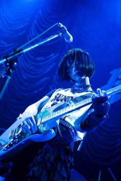 a woman holding a guitar on stage with microphones in the background and blue lighting behind her