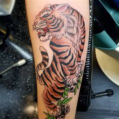 a tiger tattoo on the leg of a person's arm with flowers around it