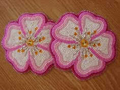 two pink and white flowers are sitting on a wooden table with beaded trimmings