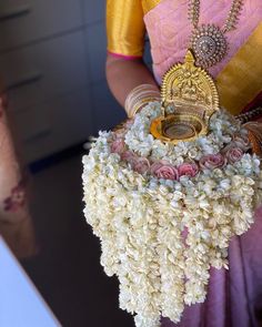 a woman in a pink and yellow sari holding a vase with flowers on it