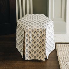 a white and blue ottoman cover sitting on top of a wooden floor next to a rug