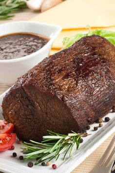 a piece of meat sitting on top of a white plate next to a bowl of sauce