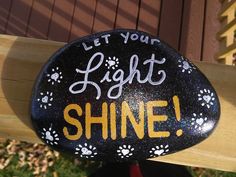 a painted rock that says let your light shine with paw prints and paws on it