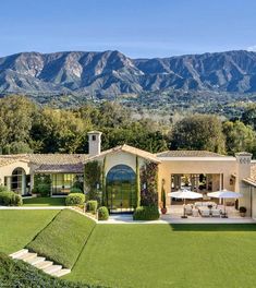 a house with mountains in the background and green grass on the lawn, surrounded by trees