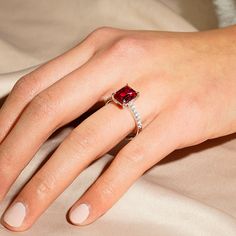 a woman's hand wearing a ring with a red stone in the middle and white diamonds around it