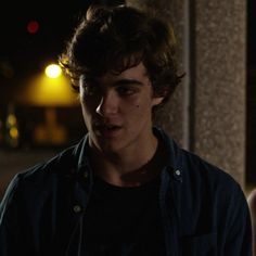 a young man standing in front of a building at night with his eyes closed and one hand on his hip