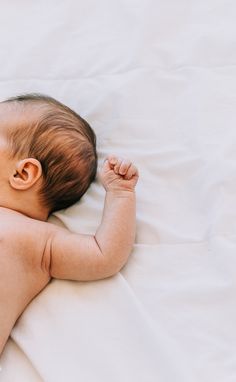 a baby laying on top of a white bed next to a pillow with its head resting on it's arm