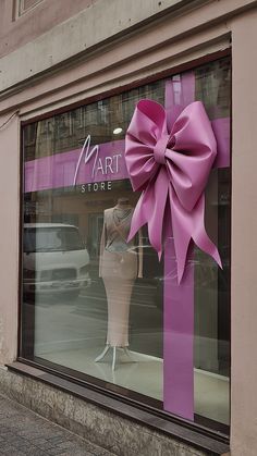 a store window with a large pink bow on it's front windows display mannequins