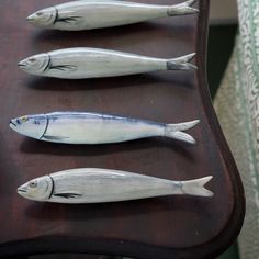 three fish on a wooden table with green curtains in the background