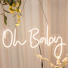 a neon sign that says old baby hanging from a chain with flowers in front of it