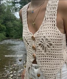 a woman standing next to a river wearing a crochet top