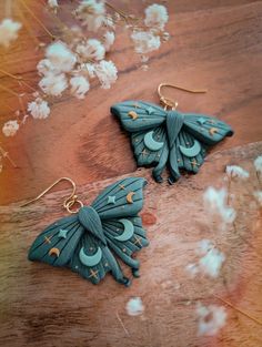 pair of earrings with blue and green designs on wooden surface next to white flower petals