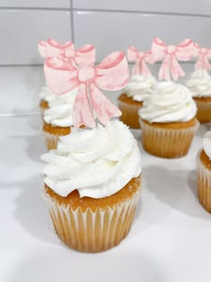 cupcakes with white frosting and pink bows on them are arranged in a row