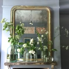 vases and flowers on a shelf in front of a mirror